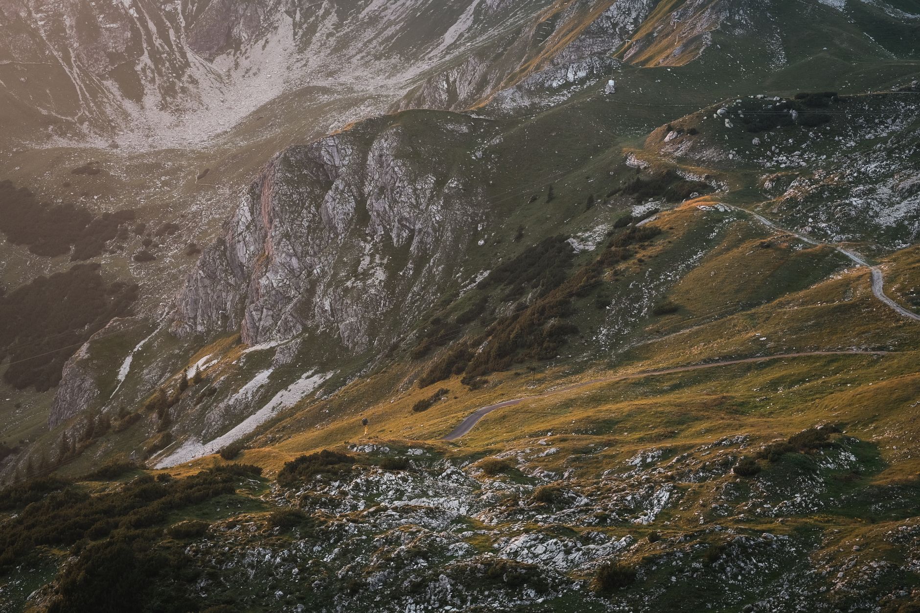 Breathtaking aerial view of a rugged mountain landscape at sunset, with winding trails and lush greenery.