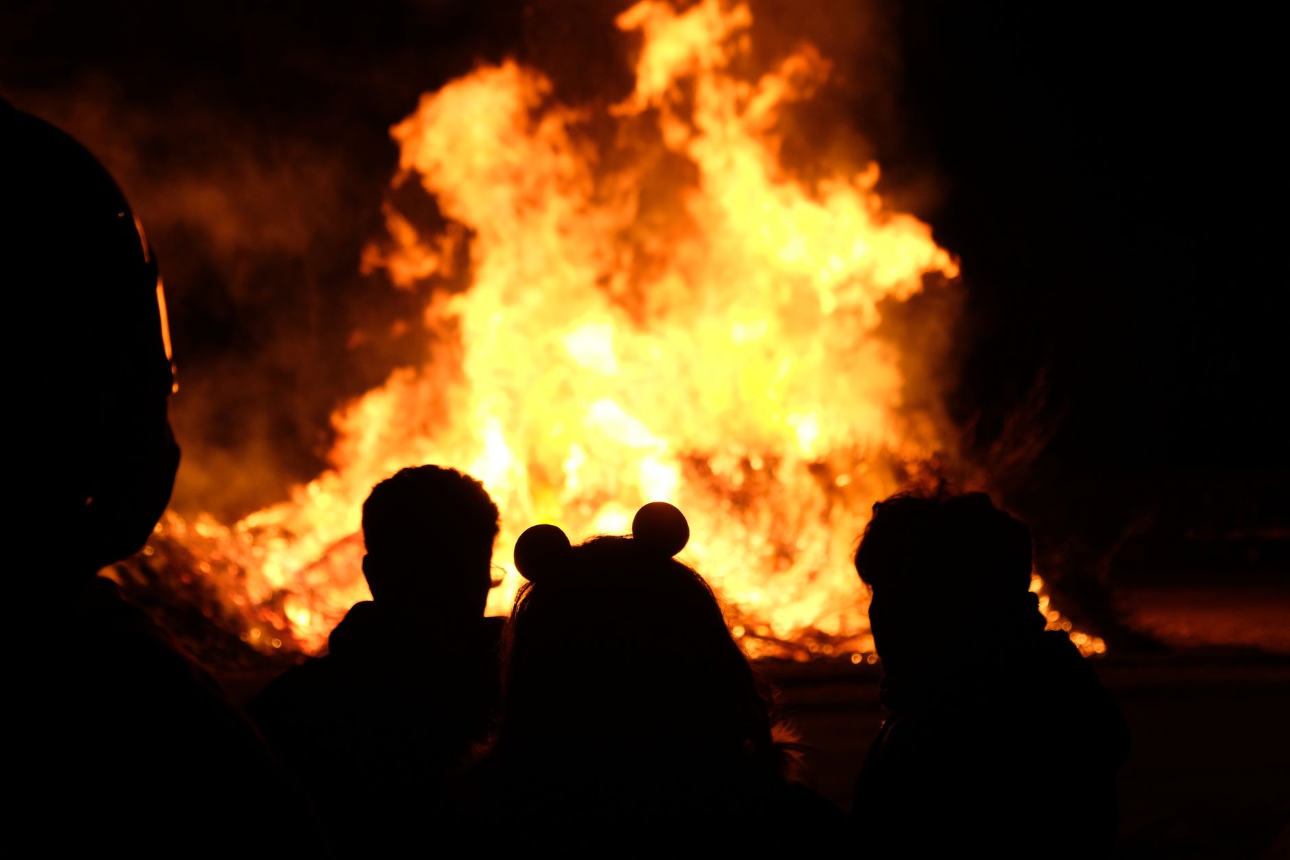Silhouetted people observing a large bonfire outdoors at night in Torino, Italy.