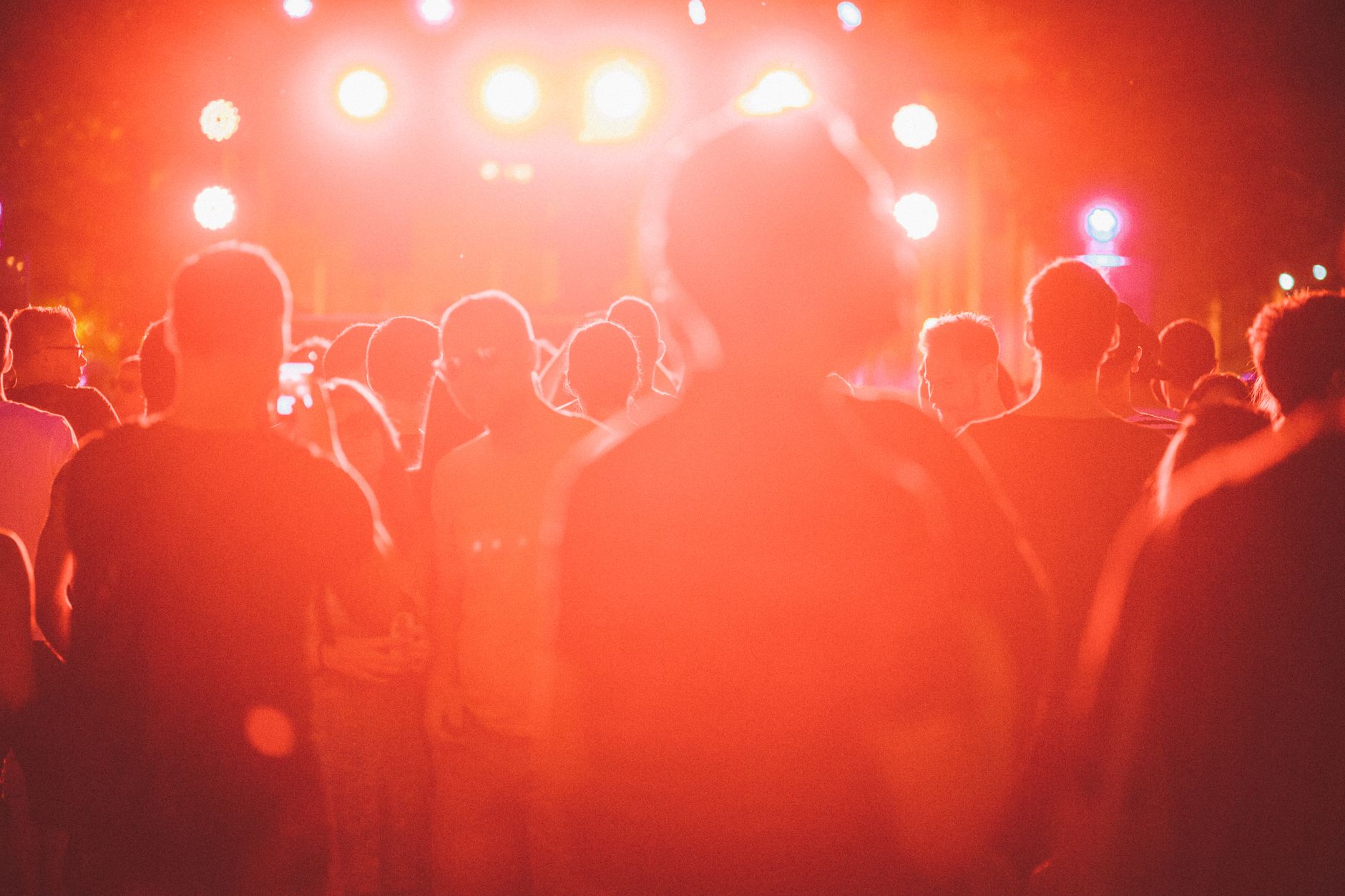 Backlit crowd enjoying a lively outdoor festival with vibrant lighting.